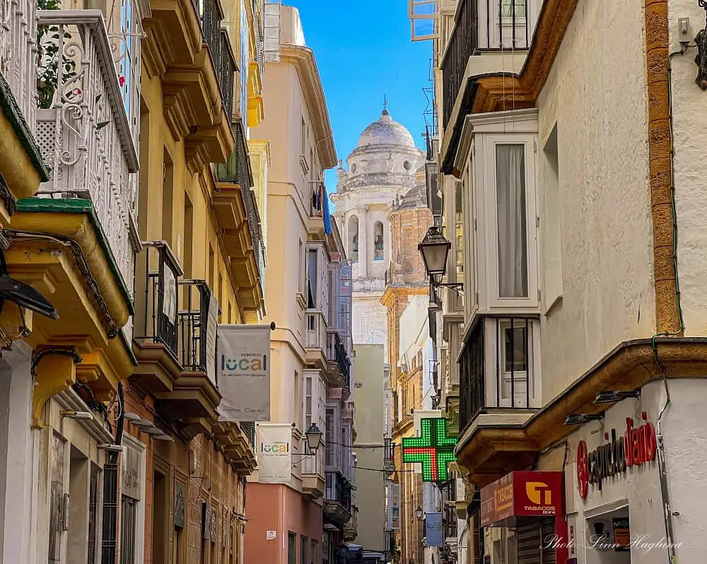 a narrow street in Cadiz Old Town with beautiful architecture and a tower with a dome at the end of the street
