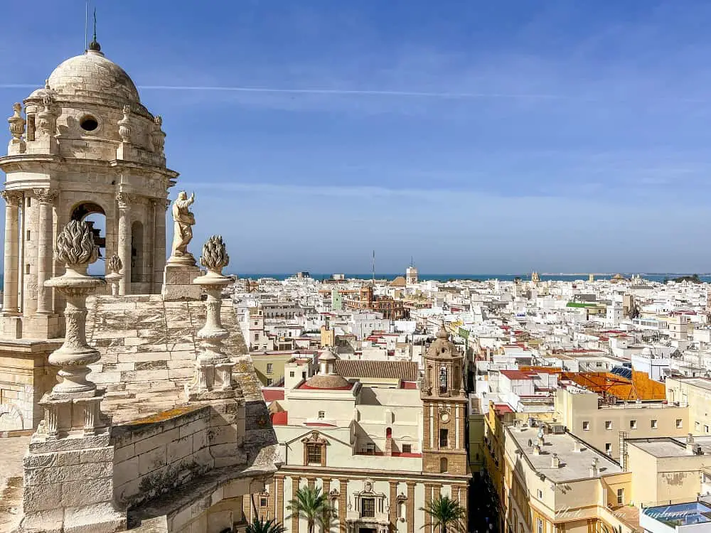 views from the belltower of Cadiz cathedral with beautiful statues on the cathedral's rooftop and whitewashed houses stretching all the way to the deep blue sea