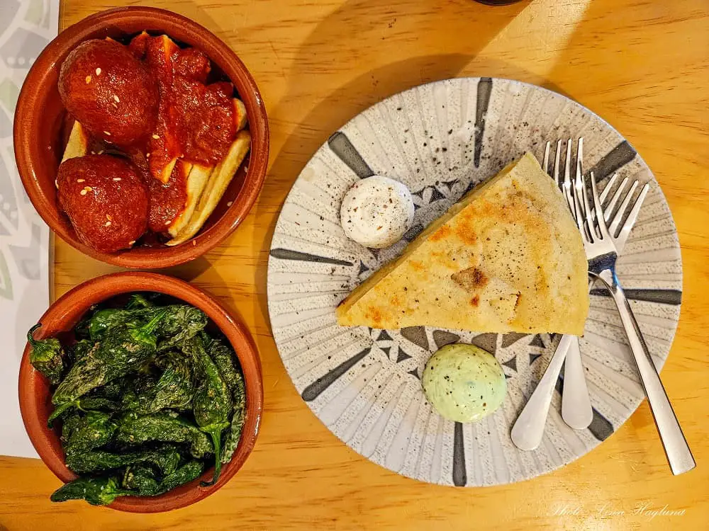 Three plates of vegan tapas Malaga. One with albondigas, one with pimientos al padron, and one with tortilla de patatas.