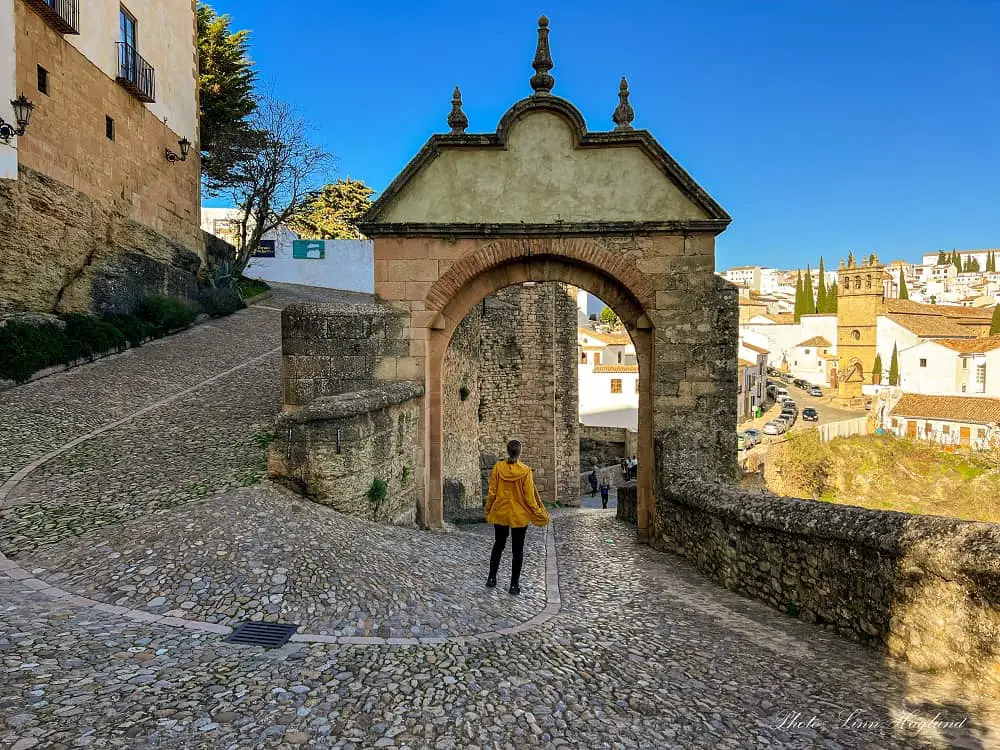 Me strolling through an old stone arch on a cobbled street which is one of the best things to do in Ronda Spain