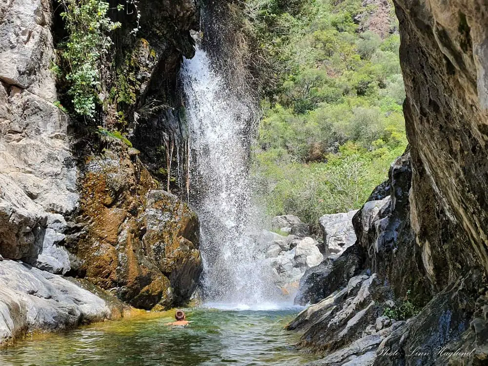 A boy swimming towards a large waterfall in Charco del Canalón.