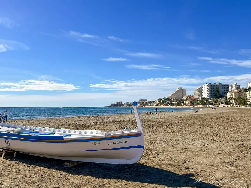 Is Benalmadena Spain worth visiting - beautiful beach with a white and blue wooden boat in the foreground.