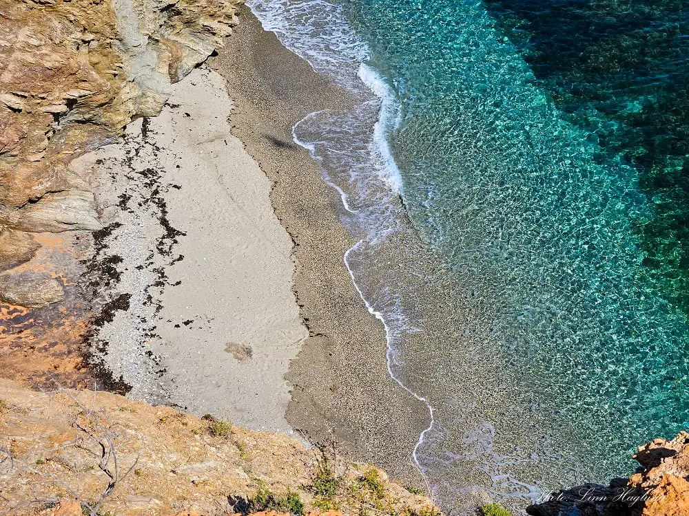 Secluded beach at the bottom of a cliff with turquoise water seen from above.