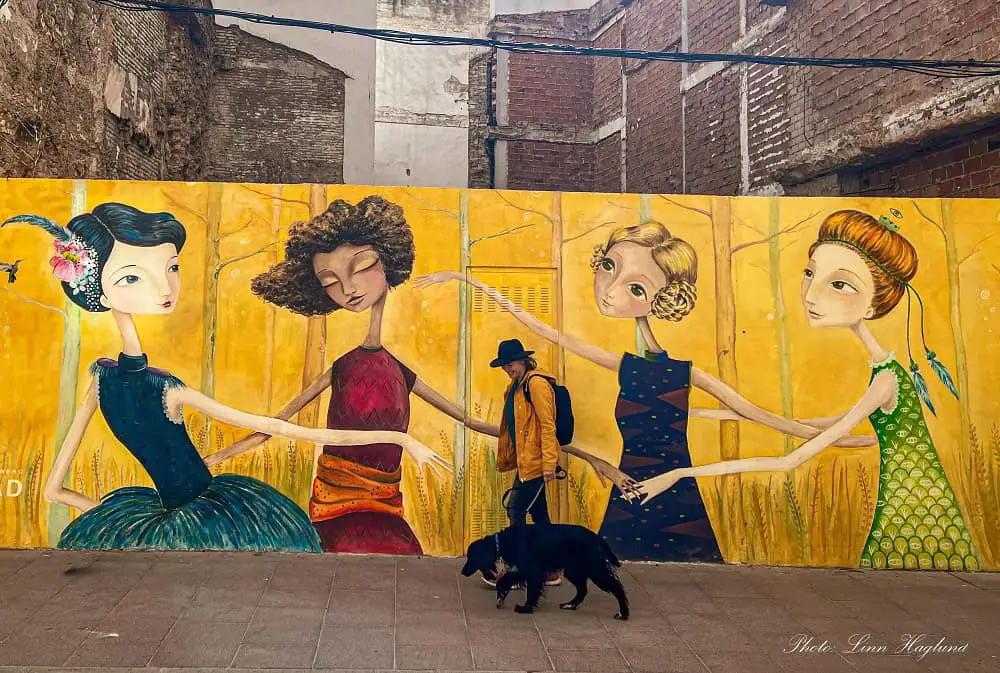 Me and my dog, Ayla, walking in front of Street art in Lucena of four ladies holding hands and a yellow background.